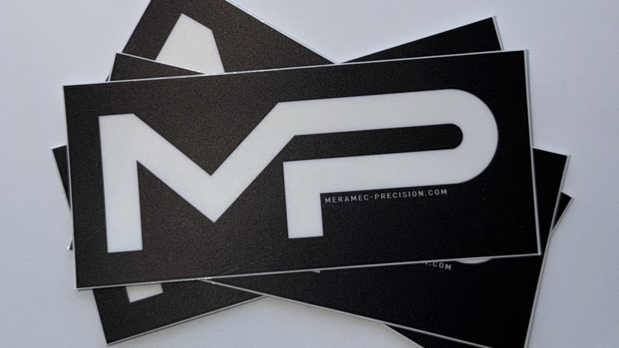 Several Meramec Precision logo stickers stacked for display